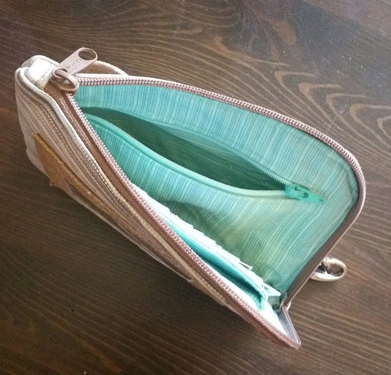 Pode incluir: Uma bolsa com z&iacute;per de listras marrons e bege com um forro turquesa. A bolsa est&aacute; aberta e o z&iacute;per &eacute; vis&iacute;vel.