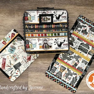 Op de afbeelding: Drie handgemaakte opbergzakken van stof met zwarte bies en ritsen. De zakken hebben een witte achtergrond met kleurrijke illustraties van naai- en knutselbenodigdheden. De tekst "Take Courage" en "Your Painter's Book" staat op de zakken gedrukt.