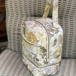Puede incluir: Una bolsa de mano con cremallera de color beige y marr&oacute;n con estampado floral y asa superior. La bolsa tiene dos compartimentos con cremallera y un forro con estampado floral.