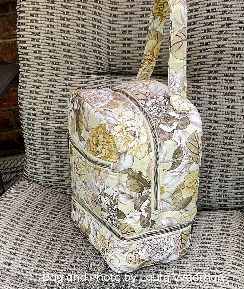 Puede incluir: Una bolsa de mano con cremallera de color beige y marr&oacute;n con estampado floral y asa superior. La bolsa tiene dos compartimentos con cremallera y un forro con estampado floral.