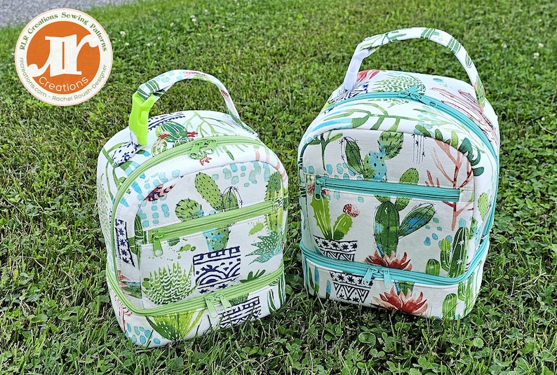 Puede incluir: Dos bolsas de almuerzo con estampado de cactus con cremalleras verdes y turquesa. La bolsa m&aacute;s peque&ntilde;a tiene una sola cremallera, mientras que la bolsa m&aacute;s grande tiene dos cremalleras. Ambas bolsas tienen un asa verde.