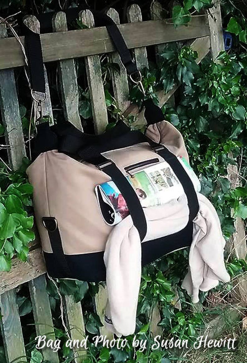 May include: A beige and black canvas tote bag with a black strap and a zippered pocket. The bag is filled with items, including a magazine and a white scarf.