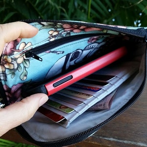 Pode incluir: Uma bolsa com z&iacute;per azul e floral com um puxador de z&iacute;per preto. A bolsa est&aacute; aberta e cont&eacute;m um telefone vermelho, cart&otilde;es de cr&eacute;dito e outros itens.