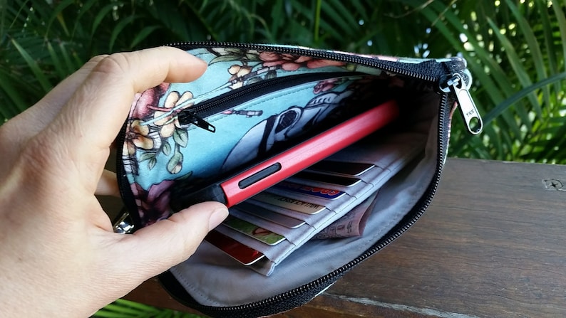 Pode incluir: Uma bolsa com z&iacute;per azul e floral com um puxador de z&iacute;per preto. A bolsa est&aacute; aberta e cont&eacute;m um telefone vermelho, cart&otilde;es de cr&eacute;dito e outros itens.