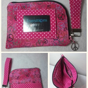 Pode incluir: Bolsa rosa com z&iacute;per com um padr&atilde;o de sinal de paz e bolinhas brancas. A bolsa tem uma janela de pl&aacute;stico transparente com um cart&atilde;o de visita que diz "Transitions". A bolsa tem uma al&ccedil;a de pulso de bolinhas rosa e brancas.