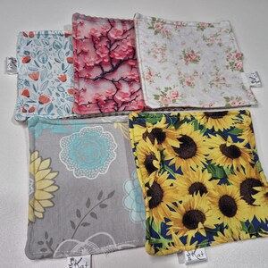 Peut inclure: Ensemble de cinq dessous de verre carrés en tissu avec différents motifs floraux. Les motifs comprennent des fleurs rouges et blanches, des fleurs de cerisier roses, des roses roses, des tournesols jaunes et des motifs floraux bleus et jaunes.