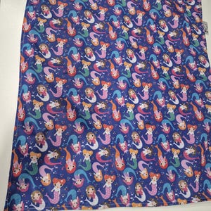 Peut inclure: Un tissu bleu avec un motif répété de sirènes de dessins animés. Les sirènes ont différentes couleurs de peau, de cheveux et de queue, notamment rose, orange et bleu. Le tissu semble être une couverture ou un textile similaire.