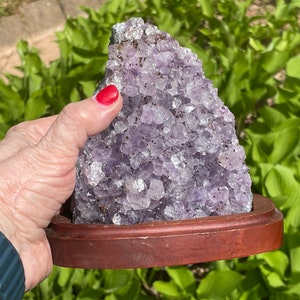 May include: A large amethyst crystal cluster with a purple and white colour, set on a wooden base.