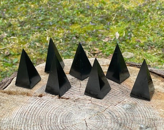 May include: Eight black obsidian pyramids arranged in a circle on a wooden surface. The pyramids are all the same size and shape.