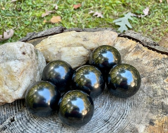 May include: Six black obsidian spheres, polished to a high shine, are arranged on a wooden surface. The spheres are smooth and reflective, with a deep black colour.