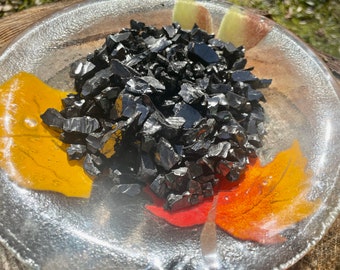 May include: A close-up of a pile of black obsidian chips in a clear glass dish with a colorful design.