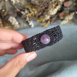 May include: A black macrame bracelet with a purple amethyst gemstone in the center.