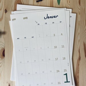 Pode incluir: Uma p&aacute;gina de calend&aacute;rio mensal em papel branco para janeiro com texto e linhas de grade em preto. O calend&aacute;rio apresenta os dias da semana rotulados MO, DI, MI, DO, FR, SA, SO e datas numeradas de 1 a 31. Um grande n&uacute;mero 1 verde est&aacute; impresso no canto inferior direito.