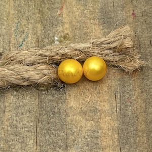 May include: Two bright yellow pearl beads on a rustic brown background.