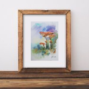 K&ouml;nnte beinhalten: Aquarellmalerei von drei rotkappigen Pilzen mit wei&szlig;en Punkten, vor einem Hintergrund aus Blau-, Gr&uuml;n- und Lilat&ouml;nen. Das Kunstwerk ist in einem Holzrahmen gerahmt und zeigt ein von der Natur inspiriertes Thema.
