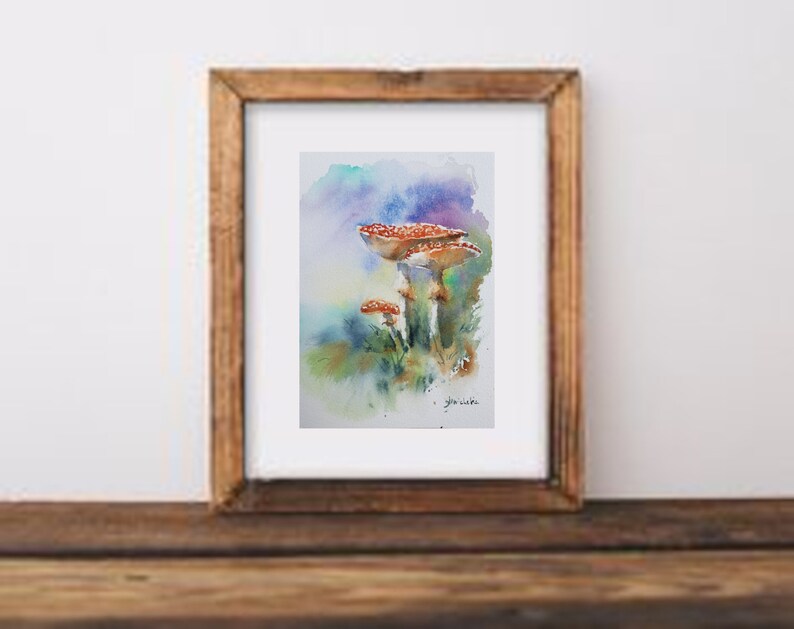 K&ouml;nnte beinhalten: Aquarellmalerei von drei rotkappigen Pilzen mit wei&szlig;en Punkten, vor einem Hintergrund aus Blau-, Gr&uuml;n- und Lilat&ouml;nen. Das Kunstwerk ist in einem Holzrahmen gerahmt und zeigt ein von der Natur inspiriertes Thema.