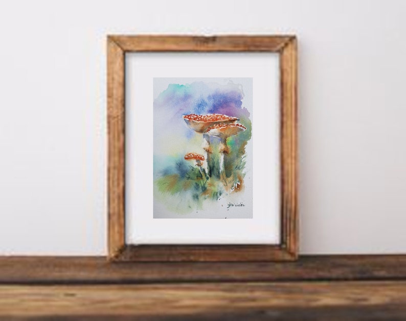 K&ouml;nnte beinhalten: Aquarellmalerei von drei rotkappigen Pilzen mit wei&szlig;en Punkten, vor einem Hintergrund aus Blau-, Gr&uuml;n- und Lilat&ouml;nen. Das Kunstwerk ist in einem Holzrahmen gerahmt und zeigt ein von der Natur inspiriertes Thema.