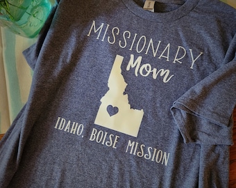Puede incluir: Una camiseta gris con el texto "Missionary Mom" y un contorno del estado de Idaho con un corazón en el centro. El texto "Idaho, Boise Mission" está debajo del contorno del estado.