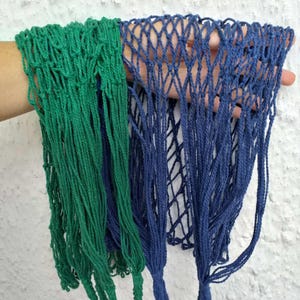 May include: Two string bags, one green and one blue, hanging together. The bags are made of a mesh material and have a knotted design.