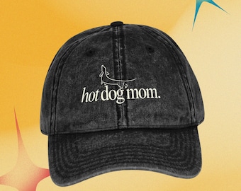 Puede incluir: Gorra de béisbol negra con el texto "hot dog mom" en escritura blanca. La gorra presenta una ilustración de perro salchicha encima del texto. El sombrero está hecho de una tela lavada y texturizada y tiene una visera curva.