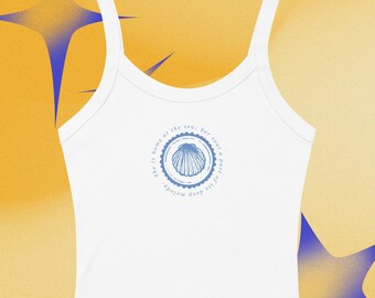 Puede incluir: Camiseta sin mangas blanca con tirantes finos. Un diseño circular azul presenta una concha y el texto "She is home at the sea; her soul a part of its deep melody."