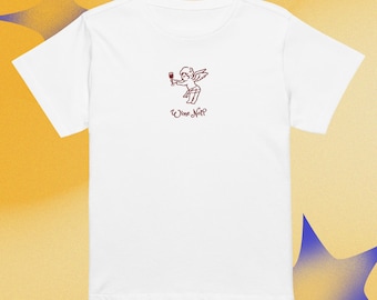 Puede incluir: Camiseta blanca con cuello redondo con una ilustración en rojo de un ángel sosteniendo una copa de vino. El texto "Wine Not?" está escrito debajo de la ilustración en cursiva.