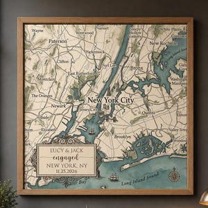 May include: A square framed map of New York City featuring a vintage aesthetic with beige land and teal water. A decorative rectangular plaque in the lower left corner displays the text: LUCY & JACK engaged NEW YORK, NY 11.25.2026.