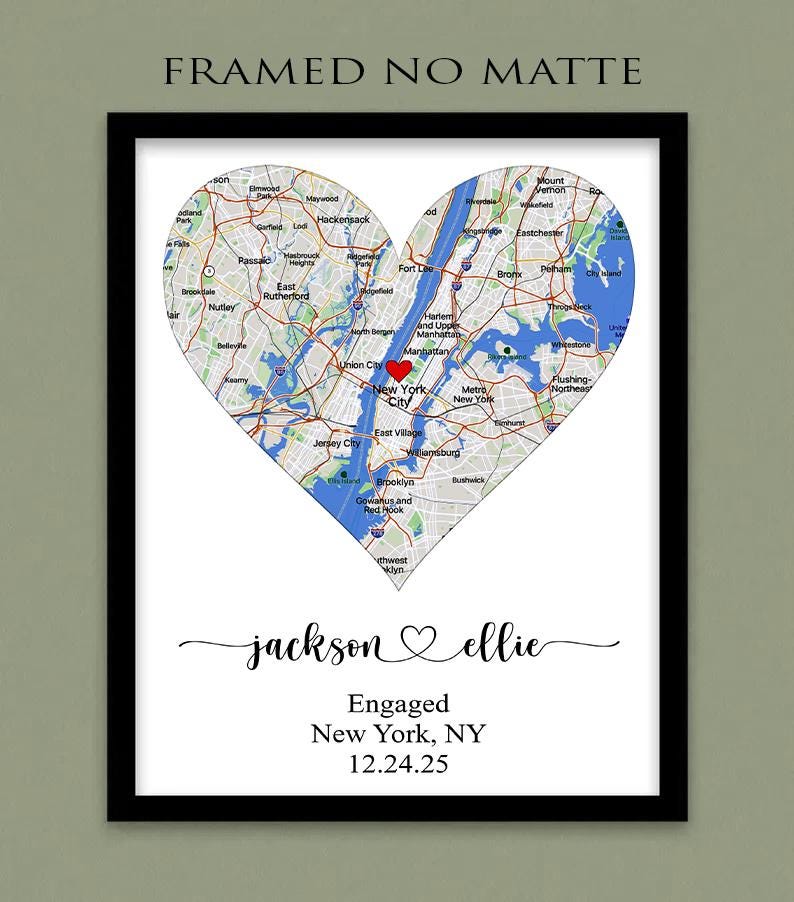 May include: A framed map of New York City shaped like a heart with a red heart icon over Manhattan. Below the map, the text reads: jackson ♡ ellie, Engaged, New York, NY, 12.24.25. The top of the image includes the text FRAMED NO MATTE.