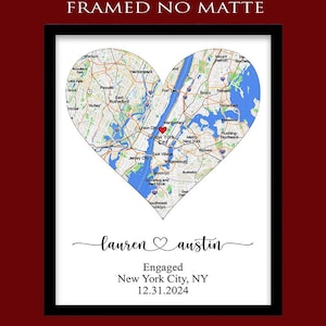 May include: A framed print featuring a heart-shaped map of New York City with a red heart icon over Manhattan. Below the map, the text reads: "lauren ♡ austin", "Engaged", "New York City, NY", and "12.31.2024". The top text reads: "FRAMED NO MATTE".