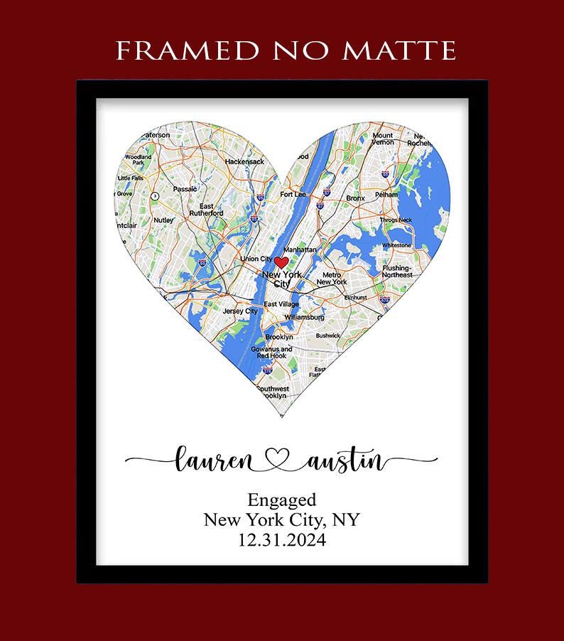 May include: A framed print featuring a heart-shaped map of New York City with a red heart icon over Manhattan. Below the map, the text reads: "lauren ♡ austin", "Engaged", "New York City, NY", and "12.31.2024". The top text reads: "FRAMED NO MATTE".