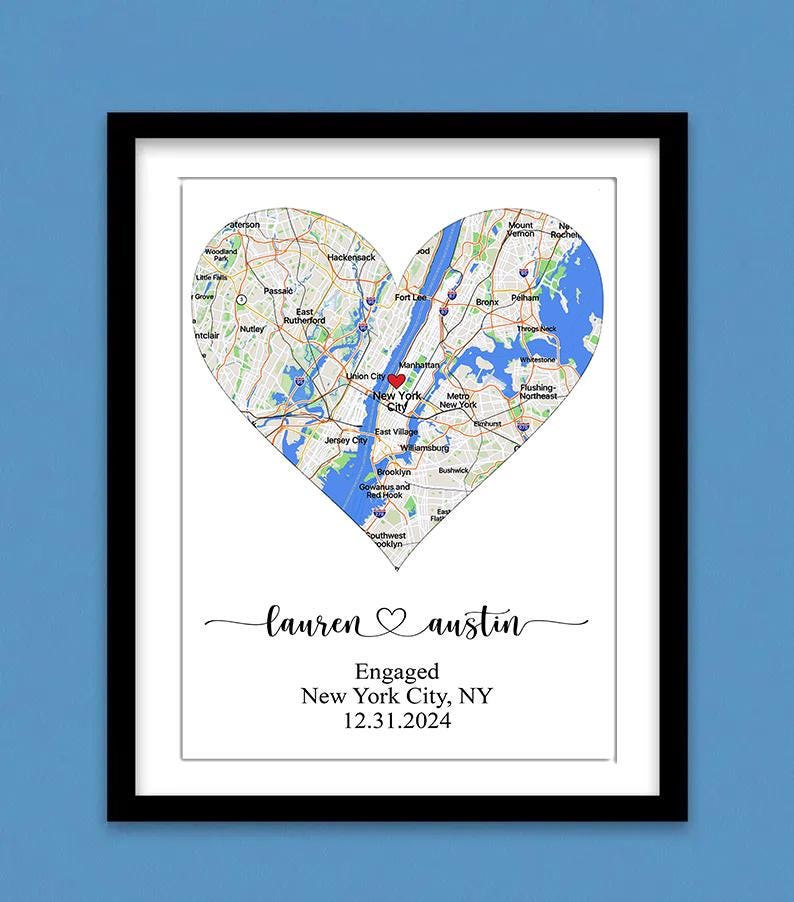May include: A framed print featuring a heart-shaped map of New York City with a red heart icon over Manhattan. Below the map, the text reads "lauren ♡ austin", "Engaged", "New York City, NY", and the date "12.31.2024" in black serif font.
