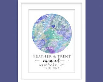 May include: A watercolor map of New York City with a blue heart marking the location. The text "HEATHER & TRENT engaged NEW YORK, NY 12.31.2022" is below the map. The image is framed in a white frame.