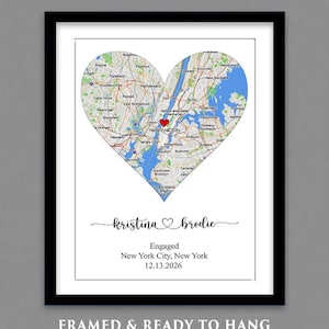 May include: A framed print featuring a heart-shaped map of New York City with a red heart icon over Manhattan. Below the map, the text reads "kristina ♡ brodie", "Engaged", "New York City, New York", and "12.13.2026". The print has a white matte and black frame.