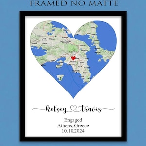 May include: A framed print featuring a heart-shaped map of the Athens, Greece region with a red heart icon over the city. Below the map, the text reads "kelsey" and "travis" with a heart symbol, followed by "Engaged", "Athens, Greece", and "10.10.2024".