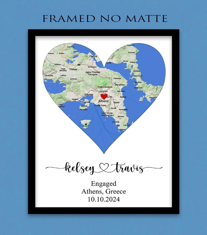 May include: A framed print featuring a heart-shaped map of the Athens, Greece region with a red heart icon over the city. Below the map, the text reads "kelsey" and "travis" with a heart symbol, followed by "Engaged", "Athens, Greece", and "10.10.2024".