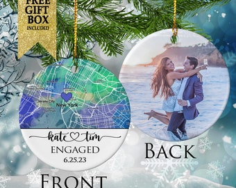 May include: A round, white, ceramic ornament with a map of New York City on the front. The map is in shades of blue, green, and purple. The text "katetim" is written in cursive with a heart symbol between the names. The text "ENGAGED" is written below the names, and the date "6.25.23" is written below that. The back of the ornament features a photo of a couple on a beach. The text "BACK" is written below the photo.