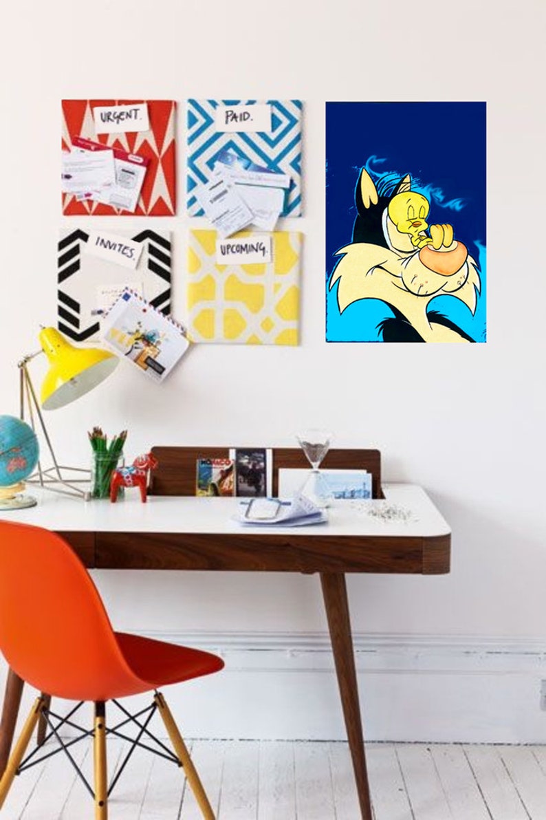 May include: A white desk with a brown wood top and legs. A red chair is in front of the desk. A yellow lamp is on the desk with a globe and a small wooden horse. There are four framed pieces of paper on the wall behind the desk. The paper is decorated with geometric patterns and the words 'Urgent', 'Paid', 'Invites', and 'Upcoming'. A cartoon image of a cat and bird is on the wall above the desk.