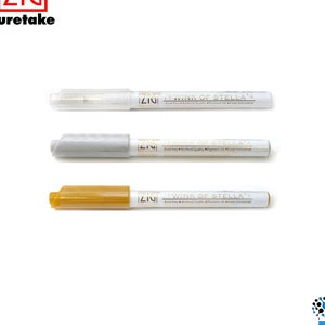 Peut inclure: Trois marqueurs métalliques avec des fûts blancs et des inscriptions dorées. Les marqueurs sont étiquetés "ZIG Wink of Stella" et sont de couleur argent, or et blanc.