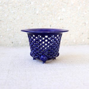 May include: A deep cobalt blue ceramic planter featuring a wide, flared rim and a delicate, intricate lattice-work pattern throughout the body. The vessel is supported by three small, rounded feet at the base, creating a raised, open-work design.