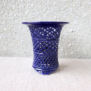 Può includere: Un vaso in ceramica blu cobalto con un motivo traforato. Il vaso ha un bordo svasato e una base arrotondata. L'intricato motivo traforato permette alla luce di passare, creando un effetto decorativo. Un elemento decorativo per la casa.
