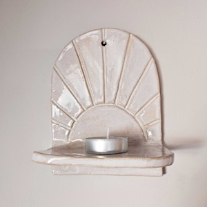 Può includere: Mensola da parete in ceramica bianca con un design a forma di sole e una piccola candela sullo scaffale.