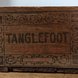 May include: A wooden box with a black and red label that reads "5 Boxes 25ft Double-Sized TANGLEFOOT Sticky Fly Paper". The label has a decorative border with black floral designs.