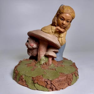 May include: A Charming Chums figurine depicting a girl and a rabbit near a mushroom. The base is decorated with leaves and the text "Charming Chums". The figurine is painted in earth tones, with the girl wearing a yellow top and blue trousers.