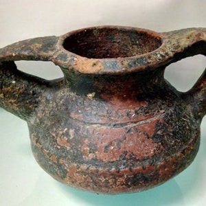 May include: A small, brown, terracotta pot with two handles. The pot has a rounded body and a wide opening at the top. The pot is decorated with a dark brown glaze.