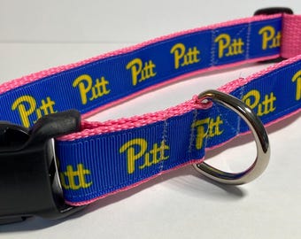 May include: A pink and blue dog collar with a repeating pattern of the word "Pitt" in yellow lettering.