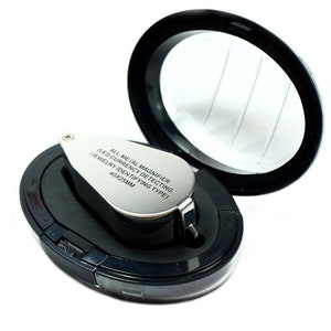 May include: A silver magnifying glass with a black handle and a black case. The magnifying glass has the text "ALL-METAL MAGNIFIER (LED CURRENCY DETECTING JEWELRY IDENTIFYING TYPE) 40X23MM" engraved on it.