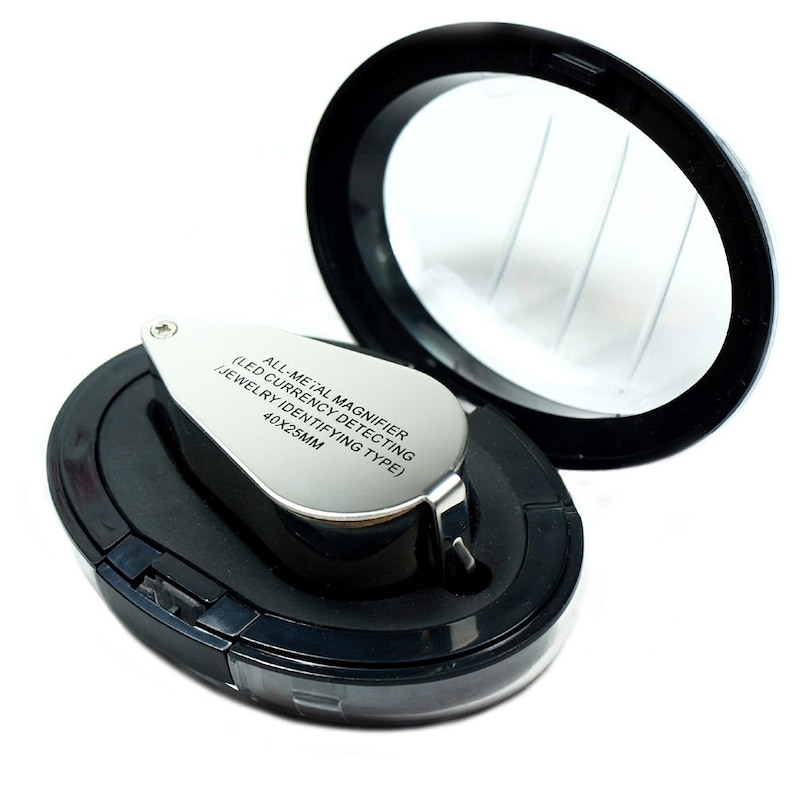 May include: A silver magnifying glass with a black handle and a black case. The magnifying glass has the text "ALL-METAL MAGNIFIER (LED CURRENCY DETECTING JEWELRY IDENTIFYING TYPE) 40X23MM" engraved on it.