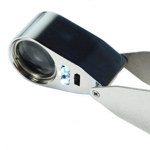 May include: A silver-colored magnifying glass with a built-in LED light. The magnifying glass has a black handle and a folding arm.