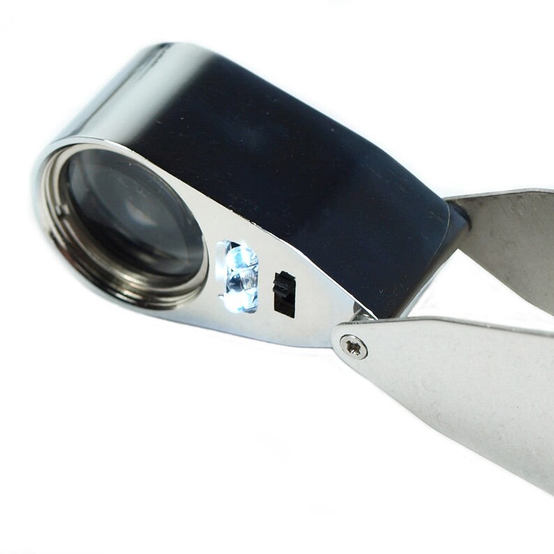May include: A silver-colored magnifying glass with a built-in LED light. The magnifying glass has a black handle and a folding arm.