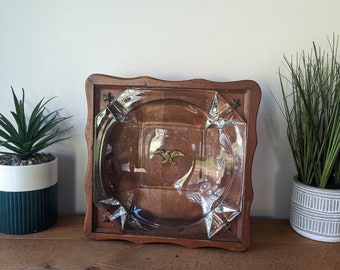 May include: A wooden ashtray with a glass insert and a gold eagle design. The ashtray is decorated with gold stars around the edge.
